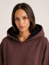Hoodie Trena de frisa color marrón chocolate, con moldería oversize, hombros caídos, capucha con cordones ajustables y bolsillo tipo canguro. Presenta puños y ruedo de rib elástico, y detalles de bordado en la manga.