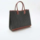Bolso tipo tote de tela a rayas verticales blancas y negras, con detalles de cuero sintético color suela en la base, manijas y bordes.