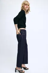Jeans de tiro medio confeccionados en denim azul oscuro, con diseño de cinco bolsillos, trabillas para cinturón y bajo deshilachado. Cierre frontal con cremallera y botón metálico.