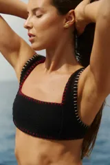 Top de bikini negro de tejido texturizado con escote cuadrado y tirantes anchos. Presenta detalles de costuras decorativas realizadas en hilo de algodón a contratono en color rojo y beige.