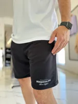 Bermuda de jogging color beige, con bolsillos laterales y estampa con texto blanco en la pierna izquierda.