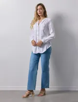 Camisa blanca de lino y rayón, con cuello a la base y escote en V abotonado. Tiene dos bolsillos con botón en el pecho y mangas largas regulables con presilla y botón.
