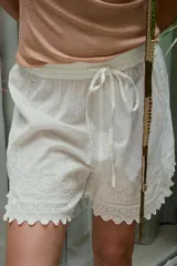 Bermuda de algodón blanca de tiro medio, con cintura elástica ajustable mediante cordón. Cuenta con delicados bordados florales y detalles de encaje a tono, con bajo acabado en ondas y aberturas laterales.
