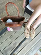 Bolso matera de cuero color marrón con doble asa de mano y correa larga desmontable. Incluye accesorio decorativo de borlas rosas y blancas.