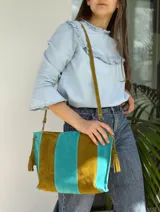 Cartera bandolera de cuero gamuzado con diseño a rayas en tonos verde oliva y turquesa. Cuenta con tiras con borlas colgantes en los laterales y una correa larga ajustable.