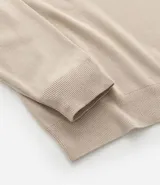 Suéter de punto con cuello redondo y manga larga, diseñado con un patrón de bloques de color en tonos beige, blanco y gris. Presenta un corte regular que se ajusta de forma anatómica al cuerpo.