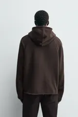 Sudadera de corte boxy fit en color marrón oscuro, con capucha, mangas largas y bandas laterales a contraste. Presenta un diseño de bajo con acabado irregular deshilachado.