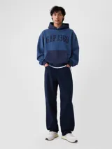 Buzo tipo canguro con capucha, de color azul con bolsillo frontal tipo canguro en un tono azul más oscuro. Presenta el logo 'GAP 1969' estampado en el pecho en color azul marino.