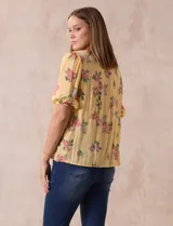 Blusa de gasa estampada con cuello a la base, escote en V plisado y lazo de ajuste. Delantera con detalles en puntilla y manga corta con puño fruncido.