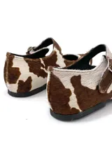 Zapato Mary Janes de cuero con estampado de vaca en tonos marrón y blanco, con correa sobre el empeine y hebilla metálica.