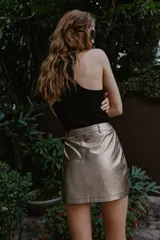 Minifalda de corte recto efecto piel en color plateado metalizado, con diseño de cinco bolsillos, trabillas para cinturón y cierre frontal con cremallera y botón metálico.