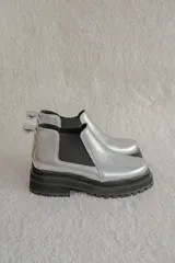 Botinetas tipo Chelsea color plateado con suela track negra de goma. Presentan elásticos laterales negros y tirador en la parte trasera.