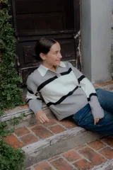 Sweater tipo polo de punto con diseño color block en tonos gris, blanco y negro. Presenta cuello camisero en contraste, cierre frontal con botones y mangas largas.