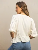 Blusa color crema con cuello redondo, abertura central con botones y mangas 3/4 con puño fruncido. Presenta detalles calados y bordados en mangas, delantera y espalda. La cintura se ajusta con un lazo.