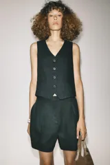 Chaleco negro con cuello en pico, sin mangas, bolsillos delanteros de vivo y cierre frontal con botones a contraste.