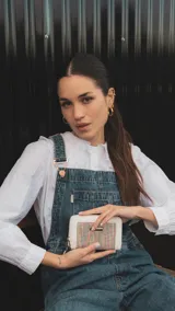 Billetera mediana con cierre perimetral, confeccionada en cuero sintético rosa y detalle central de tejido tipo telar con rayas verticales en amarillo, rosa y negro. Incluye correa de mano desmontable y placa metálica con logo de la marca.