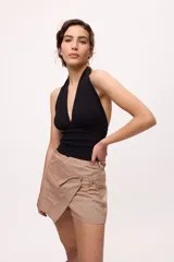 Falda short color crudo, de corte irregular y detalle de arandela dorada.