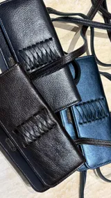 Cartera tipo bandolera de cuero metalizado en tono azulado, con diseño rectangular, solapa con cierre magnético y detalle de trenzado central. Incluye correa regulable y placa metálica con logo.