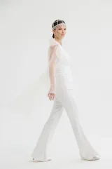 Mono largo de color blanco con diseño elegante, cuerpo entallado y mangas largas de tul con volados en los hombros. Presenta un pantalón de corte recto y fluido.