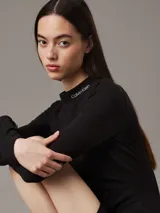 Vestido corto negro de punto milano con cuello perkins, mangas largas y corte ajustado. Logo de Calvin Klein bordado en el cuello.