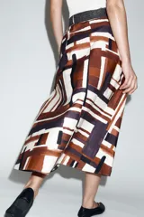 Falda midi de tiro alto en tejido de popelín con diseño evasé. Presenta un estampado geométrico en tonos tierra, crema y negro, e incluye un cinturón a juego con hebilla metálica dorada. Cuenta con cierre lateral mediante cremallera oculta.