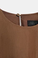Vestido mini marrón de corte evasé con diseño tipo globo en el dobladillo, cuello redondo y mangas sisa. Presenta bolsillos laterales ocultos en la costura y cierre en la espalda con pequeña abertura y botón.