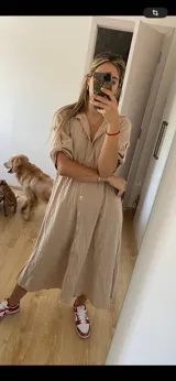 Vestido camisero midi color verde oliva, con cuello clásico, mangas cortas con trabillas y botones dorados, y cierre frontal con botones dorados.