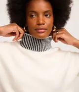 Suéter de punto pesado color blanco con cuello alto, puños y ruedo acanalados en contraste con rayas negras. Presenta diseño de hombros caídos y manga larga.