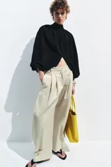 Top corto negro de punto fino, con cuello redondo y mangas largas abullonadas con pliegues.