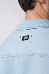 Chaqueta de denim celeste de corte relajado, con cuello clásico, cierre frontal con botones metálicos y un bolsillo aplicado en el pecho.