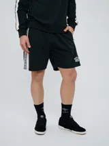 Bermuda deportiva negra Umbro, con franjas laterales en los laterales con diseño geométrico y logo bordado en la pierna.