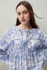 Blusa estampada de caída fluida con cuello redondo y lazos frontales, diseño con cortes horizontales y frunces, mangas largas con puños elastizados.