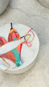 Bikini reversible de diseño triangular con tiras para atar y apliques de argollas metálicas. El conjunto presenta un estampado abstracto multicolor.