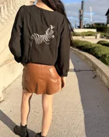 Blusa negra de corte holgado con mangas largas abullonadas y bordado de cebra en la espalda.