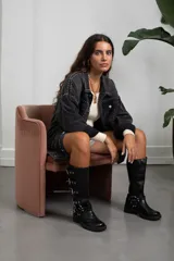 Campera de jean color negro lavado, de corte oversize, con detalle de tachas metálicas plateadas dispuestas en líneas verticales a lo largo de la prenda, cuello clásico, cierre frontal con botones metálicos y bolsillos en el pecho.