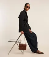 Trench coat de sastrería color negro, con cuello solapa, cierre frontal de doble botonadura y acabado satinado. Presenta un diseño estructurado y elegante.