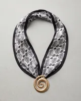 Pañuelo de seda blanco y negro con estampado paisley, bordes negros y un dije dorado en forma de espiral.