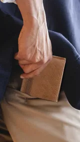 Billetera de cuero color marrón con textura granulada y detalle de franja horizontal en tono más oscuro con el logo grabado. Cuenta con múltiples compartimentos para billetes, tarjetas y visores.