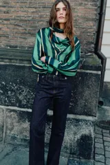 Camisa de manga larga con escote fluido tipo pañuelo, hombreras y puños abotonados. Presenta un diseño de rayas verticales en tonos verdes y amarillos.