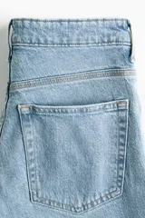 Pantalón jean de tiro alto y corte bootcut, confeccionado en denim de algodón con ligera elasticidad. Presenta diseño clásico de cinco bolsillos, cierre frontal con botón y cremallera, y perneras ligeramente acampanadas en el bajo.