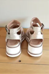 Sandalias de cuero color natural y dorado, con semi plataforma y diseño troquelado en la parte frontal. Cuentan con tira en el talón con hebilla ajustable y detalle de aplique metálico lateral.