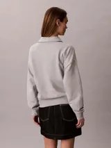 Buzo gris melange de french terry, con cuello tipo polo de media cremallera y manga larga. Presenta el logo de Calvin Klein bordado en el pecho.