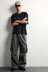 Pantalón jogger de corte relajado confeccionado en tejido de algodón compacto con elasticidad. Presenta cintura elástica ajustable con cordón, bolsillos laterales, bolsillos cargo con solapa en las piernas y detalle de pliegues en las rodillas.