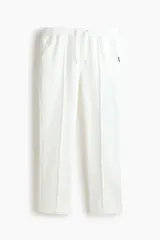 Pantalón tipo jogger de corte sastrero, color blanco, confeccionado en tejido de punto de peso medio. Presenta pliegue cosido frontal, cintura elástica con cordón de ajuste, bolsillos laterales y bolsillo trasero insertado.