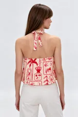 Top de viscosa con escote halter, tirantes finos, diseño holgado y estampado de motivos veraniegos en tonos rojos sobre base beige.