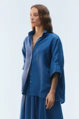 Camisa oversize blanca de lino, con corte cuadrado, mangas raglán cortas con puños anchos, aberturas laterales y cierre frontal de botones.