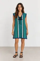 Vestido corto de tejido tipo crochet con diseño de damero en tonos azul y verde, escote en V con cordones negros para ajustar y detalles en blanco y negro.