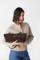 Bolso de mano tipo sobre confeccionado en cuero gamuzado color marrón chocolate. Presenta un cierre frontal metálico en tono dorado con diseño de hebilla y correa ajustable extraíble.