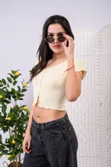 Crop top de algodón premium color amarillo pastel, con escote en V, mangas cortas y cierre frontal con botones. Presenta detalles de terminación con rulos en el ruedo y las mangas.