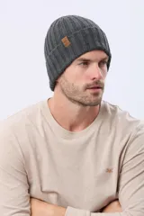 Gorro tejido de punto grueso en color gris, con diseño acanalado y etiqueta decorativa de cuero sintético en el lateral.